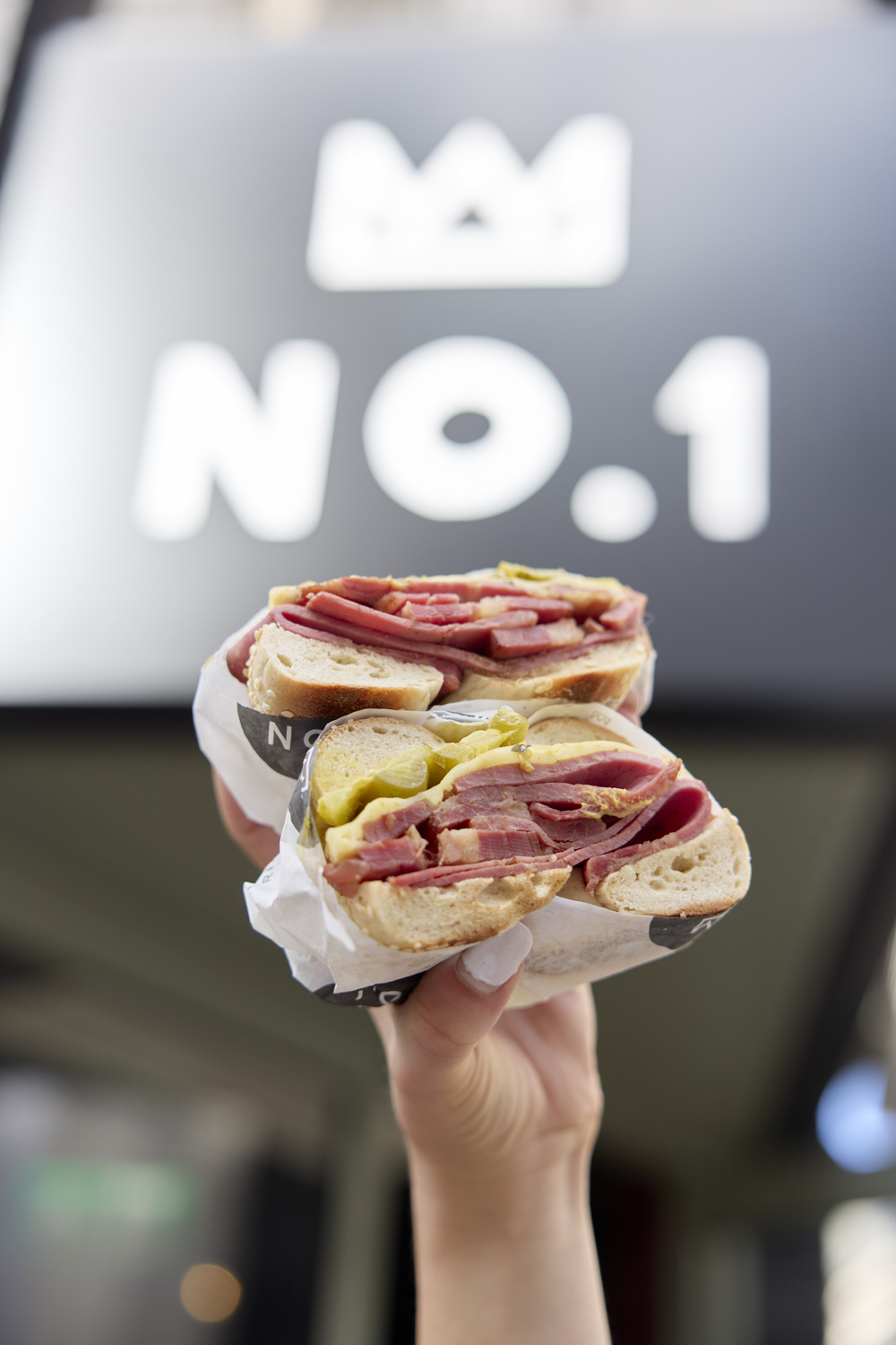 A pastrami bagel held up in front of the No.1 sign