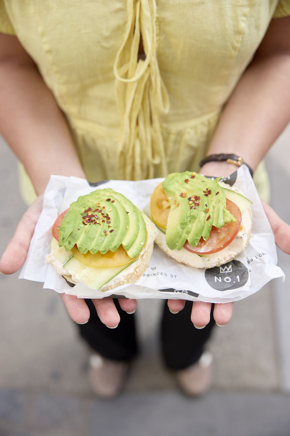 Two open avocado bagels held out on their wrapper